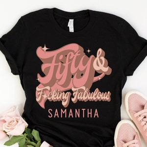 May include: Black t-shirt with a pink graphic that says "Fifty & F*cking Fabulous" with the name Samantha below it.