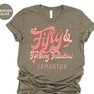 May include: A heather olive t-shirt with a pink graphic that says "Fifty & F*cking Fabulous" with the name Samantha below it.