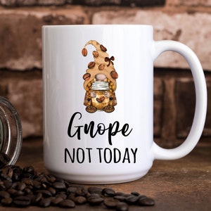 May include: White ceramic coffee mug with a brown and yellow gnome illustration holding a coffee cup. The text "Gnope Not Today" is printed on the mug.