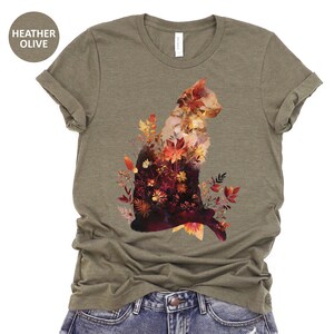 May include: Heather olive t-shirt featuring a cat silhouette filled with autumn leaves in shades of red, orange, and yellow. The shirt is made of a soft material and has a classic crew neck design. The text "HEATHER OLIVE" is in a circle.