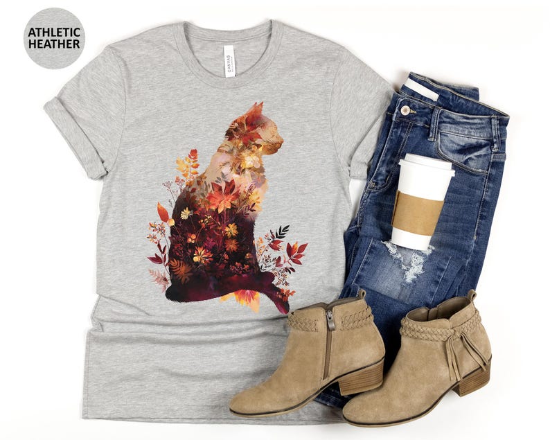 May include: A light gray t-shirt with a cat silhouette filled with autumn leaves and flowers. The shirt is paired with blue jeans, tan ankle boots, and a coffee cup. The text "ATHLETIC HEATHER" is printed on a gray circle.