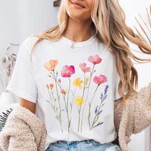 K&ouml;nnte beinhalten: Wei&szlig;es T-Shirt mit einem Aquarell-Blumenmuster mit rosa, gelben und violetten Blumen.