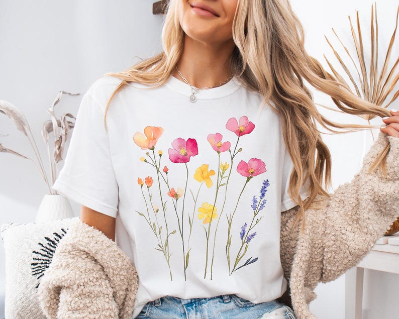 K&ouml;nnte beinhalten: Wei&szlig;es T-Shirt mit einem Aquarell-Blumenmuster mit rosa, gelben und violetten Blumen.