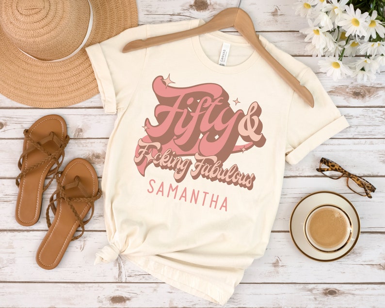 May include: A beige t-shirt with a pink graphic that says "Fifty & F*cking Fabulous" with the name Samantha underneath.