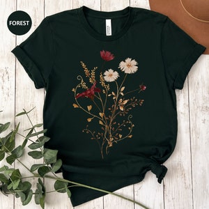 May include: A dark green t-shirt with a floral print featuring burgundy and white flowers. The flowers are arranged in a bouquet with stems and leaves.