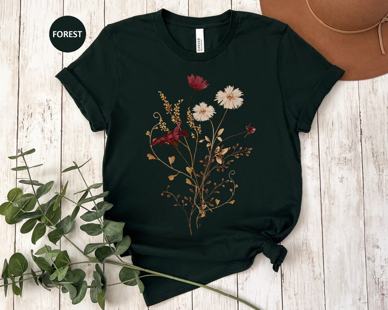 May include: A dark green t-shirt with a floral print featuring burgundy and white flowers. The flowers are arranged in a bouquet with stems and leaves.