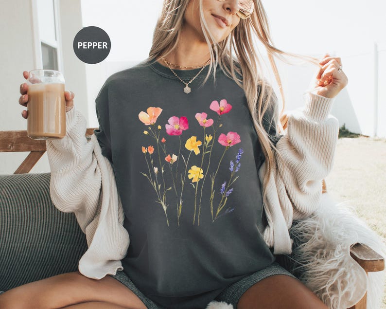 K&ouml;nnte beinhalten: Ein dunkelgraues Sweatshirt mit einem Blumendruck mit rosa, gelben und orangefarbenen Blumen. Die Blumen sind in einer Gruppe angeordnet und haben einen aquarellartigen Look. Der Text "PEPPER" ist in der oberen linken Ecke des Bildes sichtbar.