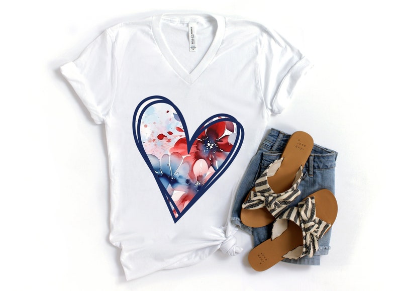 May include: White t-shirt with a blue outlined heart design featuring red, white, and blue watercolor flowers.