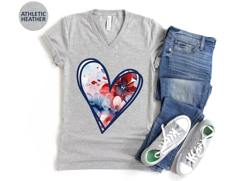 May include: A gray V-neck t-shirt with a blue outlined heart design. The heart is filled with a watercolor pattern of red, blue, and white flowers.