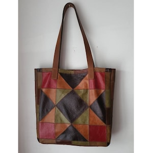May include: A brown leather tote bag with a patchwork design featuring various shades of brown, red, and green. The bag has two top handles.