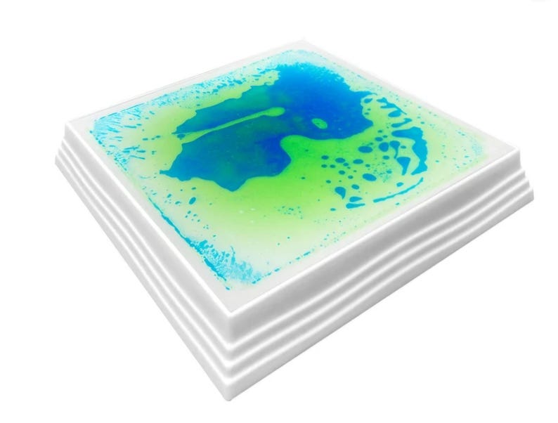 Może przedstawiać: Kwadratowa zabawka sensoryczna z białą ramką i przezroczystym płynem w środku. Płyn jest mieszanką kolor&oacute;w niebieskiego i zielonego i zawiera bąbelki.