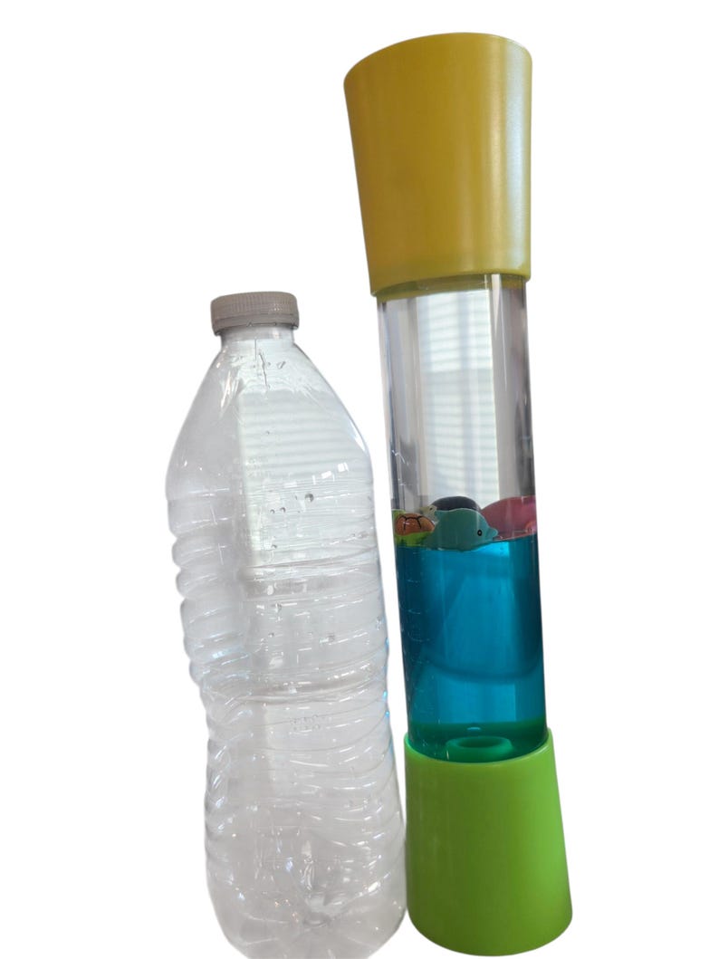 May include: A clear plastic water bottle and a tall, colorful sensory toy. The toy has a yellow top and a green base, with a clear tube filled with blue liquid and small floating objects.