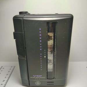 May include: A dark gray cassette recorder with the text "CASSETTE RECORDER" in purple. The recorder has a clear window to view the cassette tape and the text "VSP variable speed playback" is also visible.