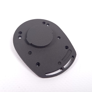 Könnte beinhalten: Ein schwarzes Kunststoffteil mit einem runden Ausschnitt und mehreren Löchern. Das Teil hat eine strukturierte Oberfläche und eine gebogene Form.