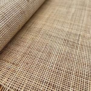 May include: A close-up of a roll of natural cane webbing, a woven material often used for upholstery and furniture making. The webbing is light brown and has a tight weave.