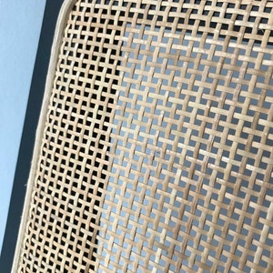 May include: Close-up of a woven cane chair seat with a black wood frame. The cane is woven in a tight, intricate pattern.