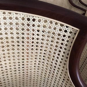Op de afbeelding: Close-up van een witte rieten stoelrug met een donkerbruin houten frame. De riet is geweven in een strak patroon, waardoor een glad en elegant oppervlak ontstaat.