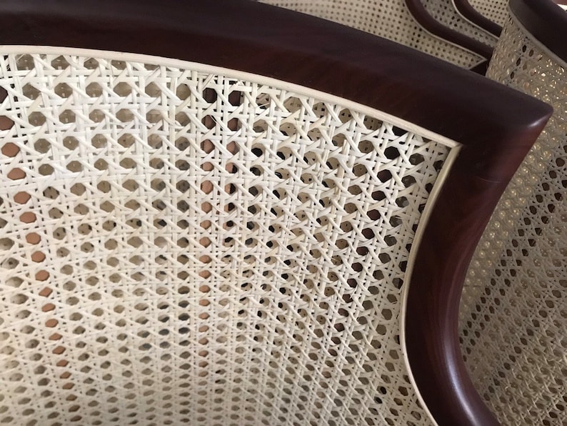 Op de afbeelding: Close-up van een witte rieten stoelrug met een donkerbruin houten frame. De riet is geweven in een strak patroon, waardoor een glad en elegant oppervlak ontstaat.