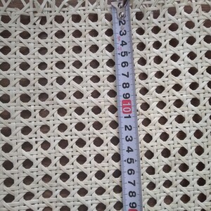 Op de afbeelding: Close-up van witte rietweving, een geweven materiaal dat wordt gebruikt voor stoelzittingen, gemeten met een meetlint. Het meetlint toont 25,4 cm.