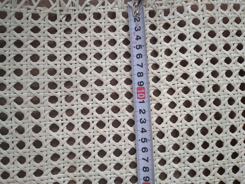 Op de afbeelding: Close-up van witte rietweving, een geweven materiaal dat wordt gebruikt voor stoelzittingen, gemeten met een meetlint. Het meetlint toont 25,4 cm.