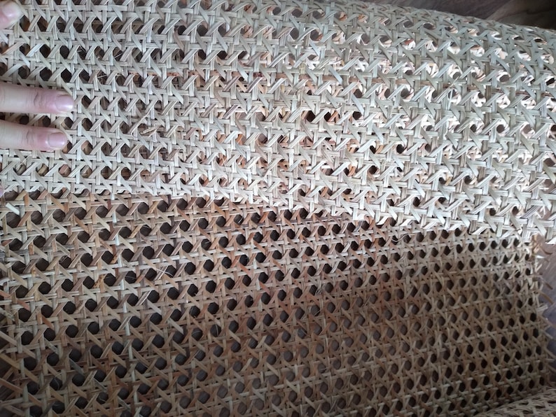 Op de afbeelding: Close-up van een geweven rietweefsel dat wordt gebruikt voor het bekleden van meubels. Het materiaal is lichtbruin en heeft een strakke weving.