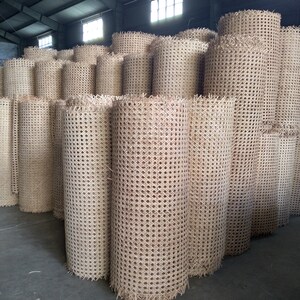 Op de afbeelding: Een grote stapel beige rietweefselrollen, gebruikt voor stoelzittingen en -rugleuningen, in een magazijn.