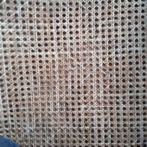 Op de afbeelding: Close-up van een geweven rieten weefsel, een materiaal dat vaak wordt gebruikt voor stoelzittingen en -rugleuningen. Het weefsel is gemaakt van natuurlijke vezels en heeft een lichtbruine kleur.