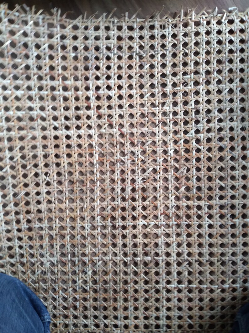 Op de afbeelding: Close-up van een geweven rieten weefsel, een materiaal dat vaak wordt gebruikt voor stoelzittingen en -rugleuningen. Het weefsel is gemaakt van natuurlijke vezels en heeft een lichtbruine kleur.