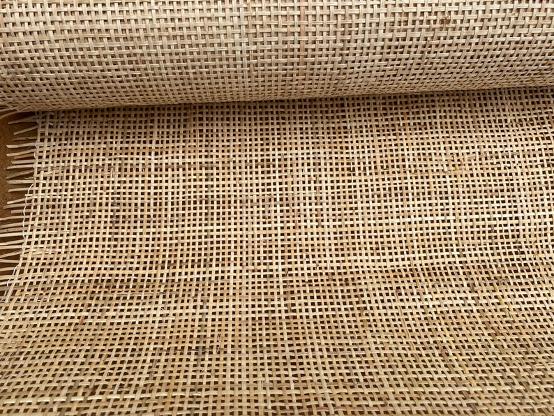 May include: A close-up of a woven cane material, often used for chair seats and other furniture. The material is light brown and has a natural, rustic look.