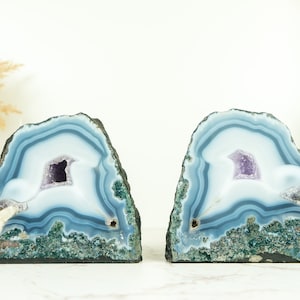 May include: A pair of blue agate bookends with amethyst crystals inside. The bookends are natural and have a rough, textured surface.