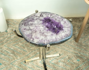 May include: A small, round amethyst table with a polished, purple and white crystal top. The table has a silver metal base with four legs.