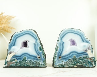 May include: A pair of blue agate bookends with amethyst crystals inside. The bookends are natural and have a rough, textured surface.