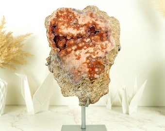 May include: A large, irregularly shaped geode with a pink and orange interior. The geode is on a metal stand.