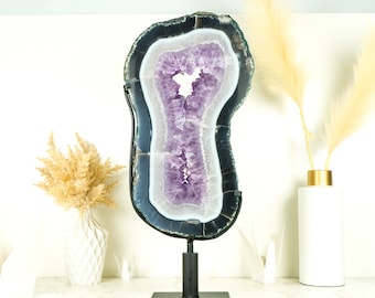 May include: A large amethyst geode slice with a black metal stand. The geode is purple and white with a natural, irregular shape.
