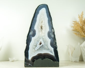 May include: A large, freeform, gray and white agate geode with a natural, rough edge. The geode is on a black base and has a white background.