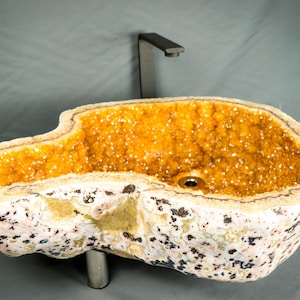 May include: A unique, natural stone sink with a yellow and white crystal interior. The sink is shaped like a large, irregular rock and has a modern, minimalist faucet.