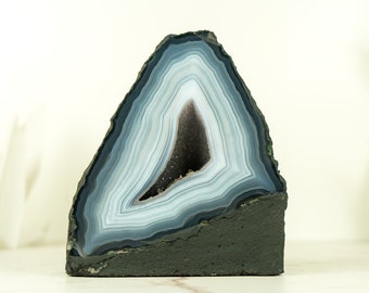 May include: A large, triangular, blue and white agate geode with a dark gray base. The geode has a natural, rough texture and is a beautiful example of the natural beauty of crystals.