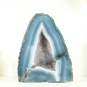 Op de afbeelding: Een grote, natuurlijke agaatgeode met een blauw en wit gebandeerd patroon. De geode is doormidden gezaagd, waardoor een hol interieur zichtbaar wordt met een paarse en witte kristalkluster.