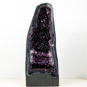 Op de afbeelding: Een grote amethistgeode met een donkerpaars interieur en een donkergrijze buitenkant. De kristalformatie is zichtbaar in de geode, met een donkerblauwe en paarse rand. De geode staat rechtop.