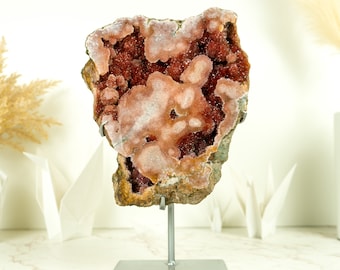 Könnte beinhalten: Ein großer, rosa-brauner Geodenkristall auf einem Metallständer. Die Geode hat eine raue Außenseite und ein glattes, kristallines Inneres.