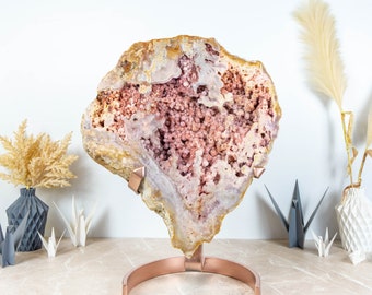 May include: A large, pink and brown geode on a copper stand. The geode has a rough, natural exterior and a smooth, crystalline interior. The geode is a beautiful example of natural beauty.