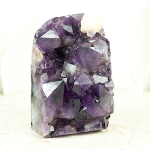 Pode incluir: Um grande aglomerado de cristais de ametista com um esquema de cores roxo e branco. O cristal é uma formação natural com muitos pontos e facetas.