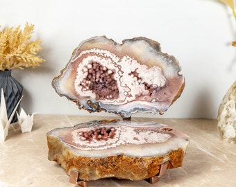 May include: A large, natural agate geode with a pink and white interior, displayed on a metal stand. The geode is cut in half, revealing the intricate crystal formations inside.