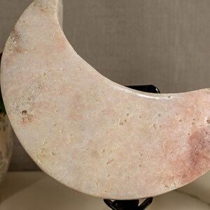 May include: A pair of pink crescent moon shaped crystal sculptures on a black metal stand. The crystals are polished and have a smooth, glossy finish.