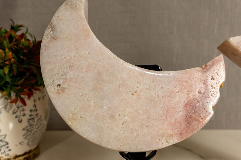 May include: A pair of pink crescent moon shaped crystal sculptures on a black metal stand. The crystals are polished and have a smooth, glossy finish.