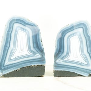 Op de afbeelding: Een paar blauwe agaat boekenleggers met een wit en grijs bandpatroon. De boekenleggers zijn gemaakt van natuursteen en hebben een gladde, gepolijste afwerking.