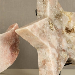 May include: Two pink crystal sculptures, one shaped like a crescent moon and the other a five-pointed star, are displayed on black stands.
