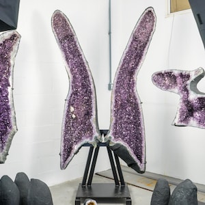 Op de afbeelding: Drie grote amethistgeoden op displaystandaards. De geoden zijn paars en hebben een kristallen structuur. De geoden staan op een witte achtergrond.