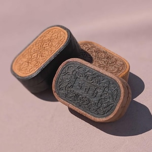 May include: Three decorative, rectangular boxes with ornate, embossed designs. The boxes have a two-tone color scheme, with a dark base and a lighter, tan-colored top. The boxes are arranged at an angle, showcasing their intricate details.