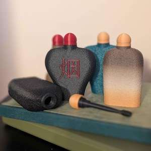 May include: A selection of decorative bottles in black, teal, and tan, with red and tan stoppers. One bottle features the Chinese character for "smoke" in red. A black, cylindrical piece and a black and tan pipe are in the foreground.